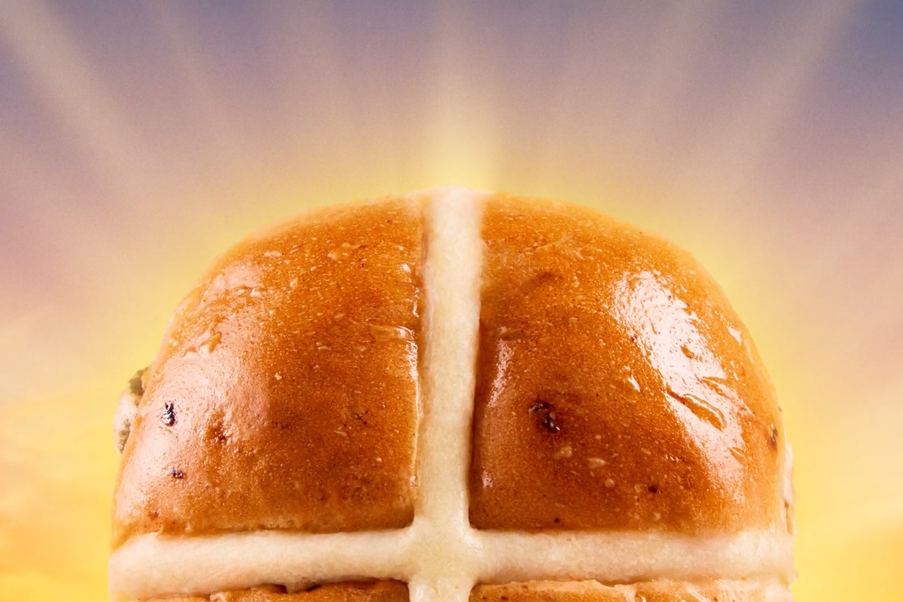 A hot cross bun backlit by the image of a rising sun