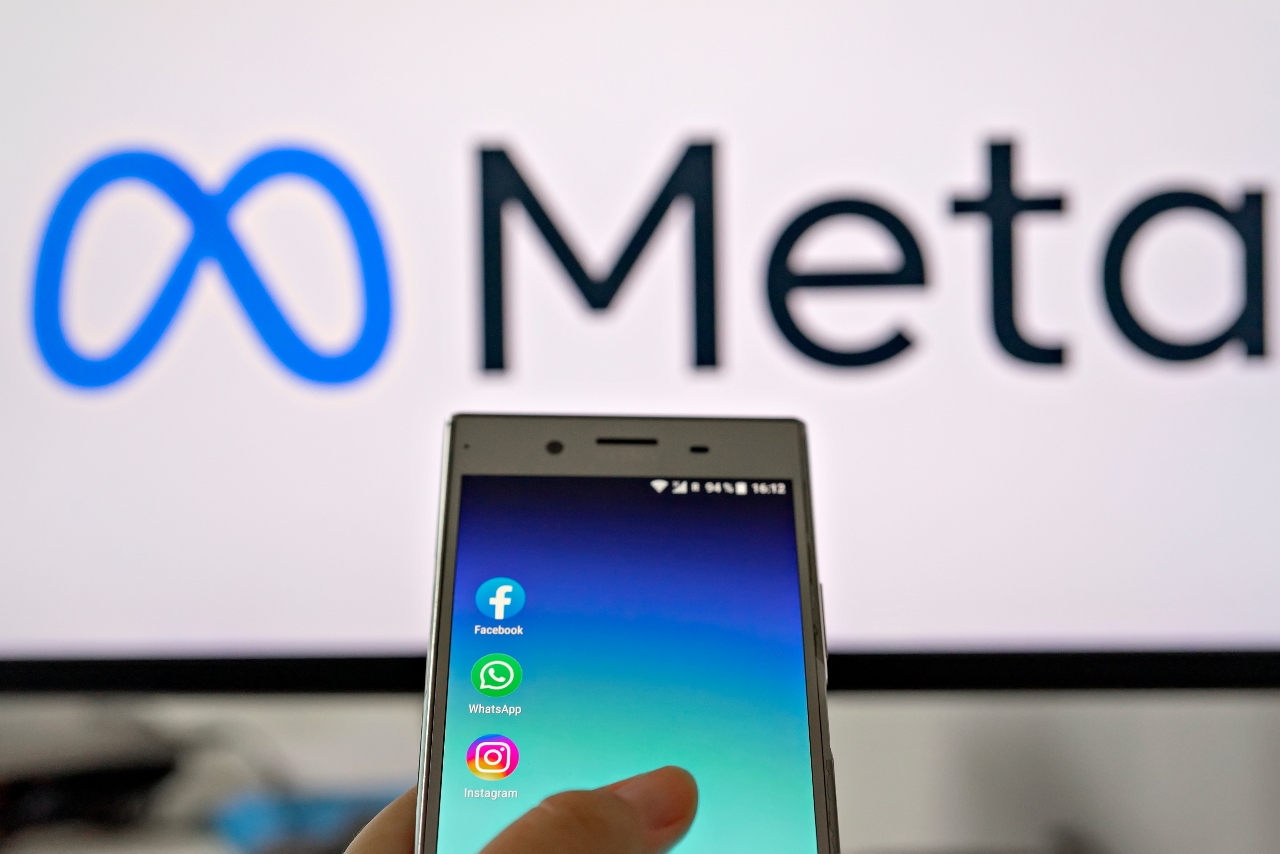 Meta logo behind a phone with the Facebook, WhatsApp and Facebook logos. 