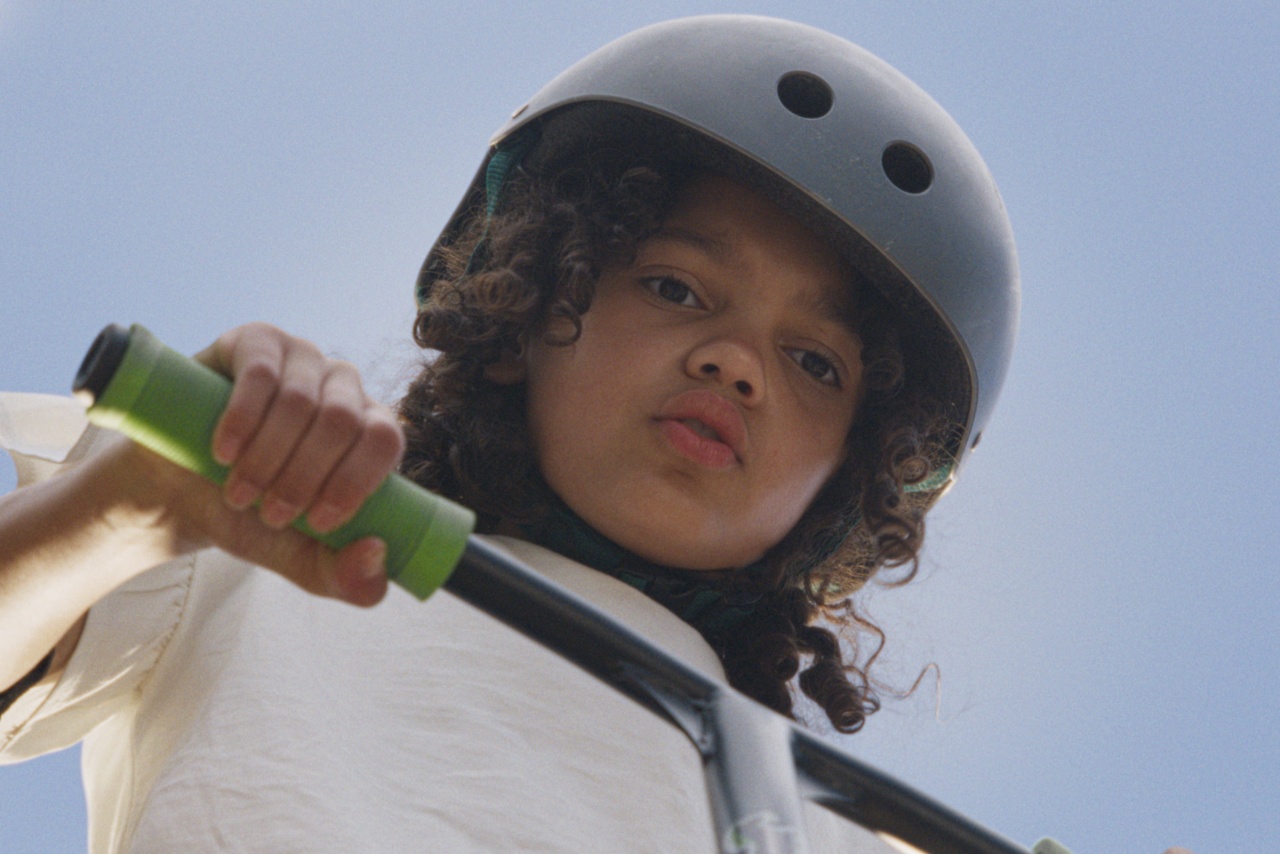 Child with long curly hair riding scooter or bike and wearing helmet